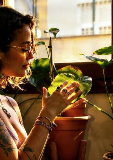 Vanesa a contraluz junto a la ventana, sosteniendo con cuidado la hoja de una planta